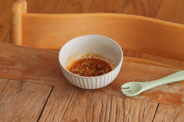 bowl containing baby food buckwheat puttane sca on a table in front of highchair with baby spoon