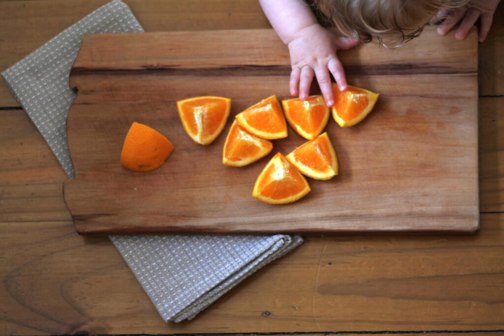 baby hand touching pieces of orange on wooden cutting board