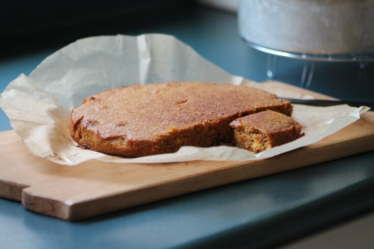 whole orange cake cut into with one piece exposed on wooden cutting board