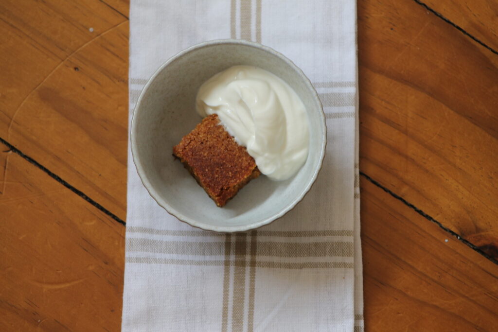 cut piece of whole orange cake in bowl with yoghurt on tea towel